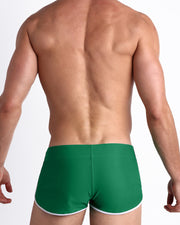 Back view of a male model wearing GREEN RUSH men’s swim shorts in a playful, vibrant green hue by the Bang! Clothes brand of men's beachwear.