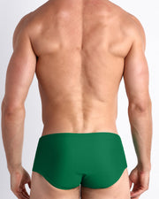 Back view of a male model wearing men’s GREEN RUSH Brazilian Sunga swimwear in a pine green color by the Bang! Clothes brand of men's beachwear.