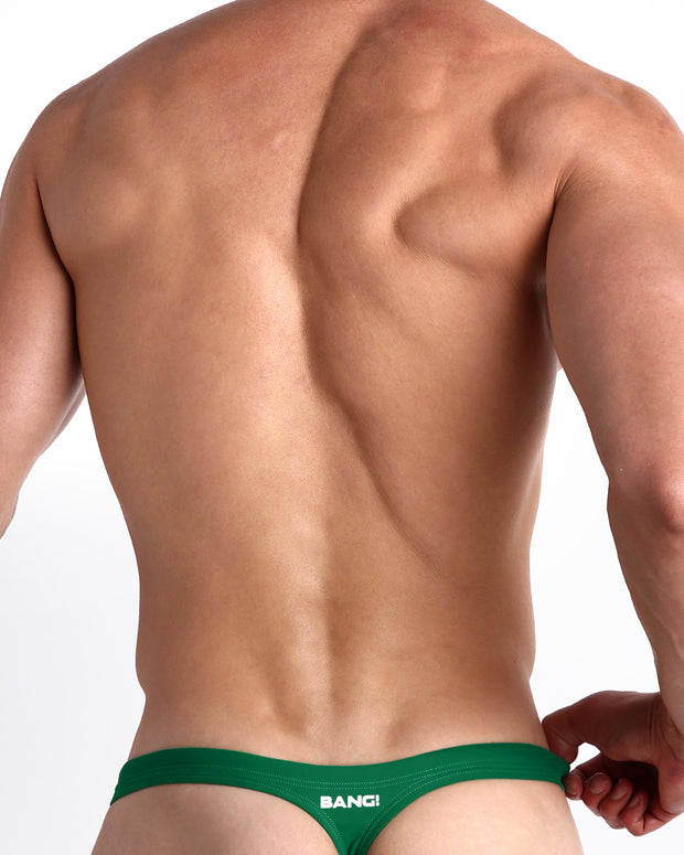 Back view of a male model wearing men’s GREEN RUSH Swim Thong in a vibrant, playful pine green color made with Italian-made Vita By Carvico Econyl Nylon with the official logo of BANG! Brand in white.