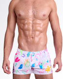 BANG I Saw The Sign Show Shorts — model wearing white show shorts featuring playful multicolor graphic illustrations including hearts, clocks, flamingos, and tropical icons with an adjustable drawstring waistband.