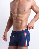 Model wearing the Imperial Blue Poolside Shorts featuring contrast red and white side stripes, elastic drawstring waistband, and zip pockets.