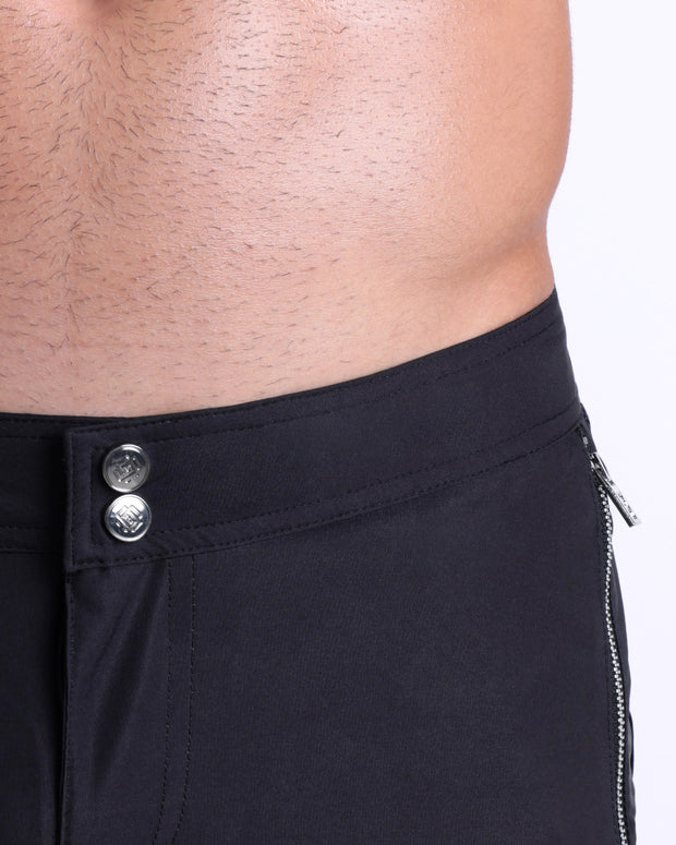 Close-up view of inseam and details of JET BLACK swimsuit for men, showing custom branded silver buttons.