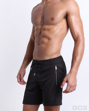 Side view of the JET BLACK for men’s summer long boardshorts with dual zippered pockets in a solid black color designed by DC2 a brand based in Miami.