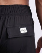 Close-up view of the JET BLACK men’s Flex Boardshorts back pocket, showing custom branded silver metal logo.