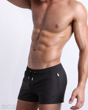 Side view of the JET BLACK swimsuit Poolside Shorts men’s shorter length shorts with side zipper pockets featuring a dark black color. These high-quality swimwear bottoms by DC2, a men’s beachwear brand from Miami.