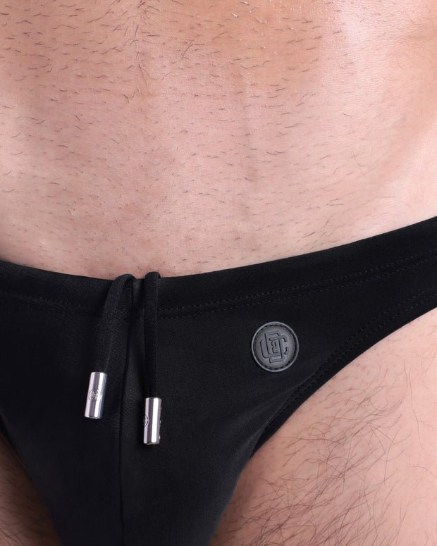 Close-up view of the JET BLACK men’s drawstring briefs showing black cord with custom branded metallic silver cord ends, and matching custom eyelet trims in silver.
