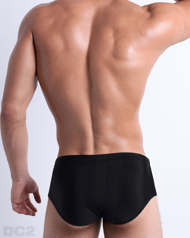 Back view of a male model wearing the JET BLACK men’s Brazilian Sunga swimwear by BANG! Miami in a solid black color.