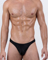 Male model wearing DC2 JET BLACK men's swim thong – sexy low-rise black bikini swimwear with sleek contour pouch for a bold beach look.