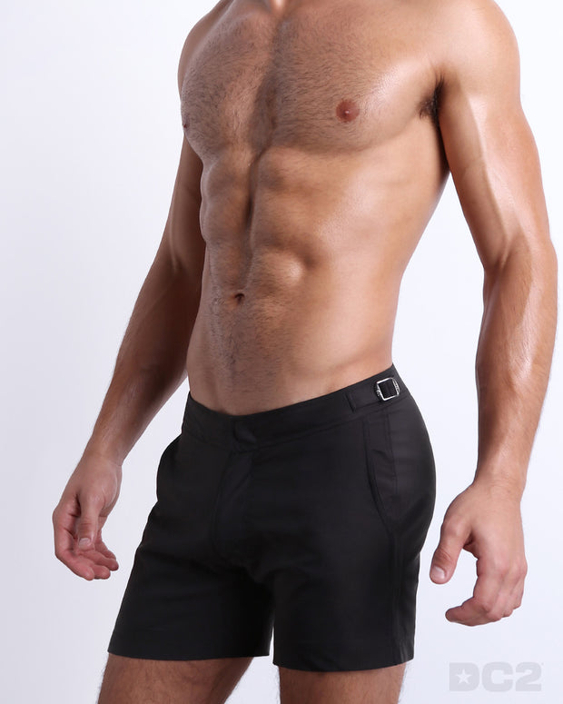 Side view of the JET BLACK swimsuit Tailored Shorts with dual pockets and adjustable side buckles for men featuring a black color is designed by BANG! Clothes in Miami.