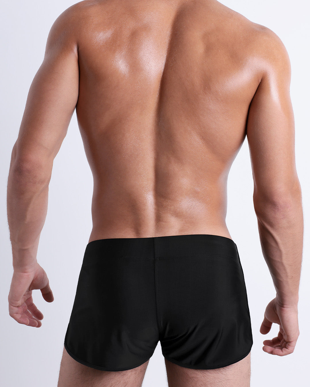 Back view of male model wearing the JET BLACK beach Swim Shorts for men by BANG! Miami in a solid black color.
