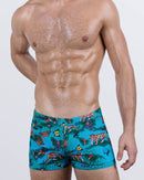 Model wearing JUNGLE BOOGIE square-cut men's swim trunks in a vivid jungle print with tigers, butterflies, and tropical florals. Made for bold beachwear statements with a body-defining silhouette and snug fit.