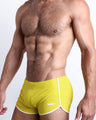 Side view of a masculine model wearing men’s swimwear in KOKOMO YELLOW a solid sunny bright yellow color made with Italian-made Vita By Carvico Econyl Nylon with official logo of BANG! Brand in white.