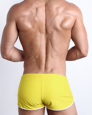 Back view of a male model wearing KOKOMO YELLOW men’s swim shorts in a yellow color made with Italian-made Vita By Carvico Econyl Nylon by the Bang! Clothes brand of men's beachwear.