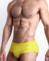 Side view of a masculine Model wearing the KOKOMO YELLOW men’s beach brazilian swimwear in a yellow color made with Italian-made Vita By Carvico Econyl Nylon with official logo of BANG! Brand in white.