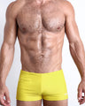 Frontal view of a sexy male model wearing men’s KOKOMO YELLOW swimsuit with mini pockets in a solid bright yellow color made with Italian-made Vita By Carvico Econyl Nylon by the Bang! Menswear brand from Miami.