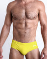 Frontal view of a sexy male model wearing the KOKOMO YELLOW Swim Brief men’s swimsuit in a bright yellow color made with Italian-made Vita By Carvico Econyl Nylon by the Bang! Menswear brand from Miami.