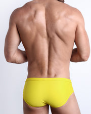 Back view of a male model wearing men’s swim briefs in KOKOMO YELLOW a solid yellow color made with Italian-made Vita By Carvico Econyl Nylon by the Bang! Clothes brand of men's beachwear.