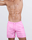 Male model wearing the LA BEACH EN ROSE Resort Shorts, premium swimwear in a solid bright light pink color for men. These high-quality swimwear bottoms by DC2, a men’s beachwear brand from Miami.