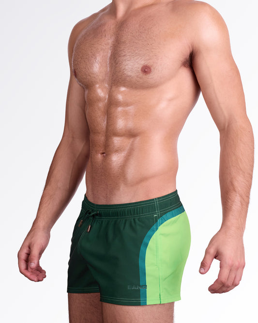 BANG Lines in Stereo Show Shorts — model wearing gradient green show shorts featuring a deep forest green base transitioning into bright lime panels with a modern color-block stripe detail and adjustable drawstring waistband.