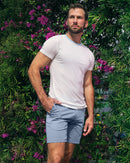Model wearing DC2 White Lotus Pima Cotton T-Shirt and Ultimate Blue Street Shorts, standing by blooming flowers, showcasing a refined and effortless resort look.