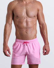 Frontal view of a sexy male model wearing men’s boardshorts in pink by the Bang! Menswear brand from Miami.