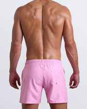 Back view of a hot male model wearing men’s boardshorts in pink by the Bang! Clothes brand of men's beachwear from Miami.