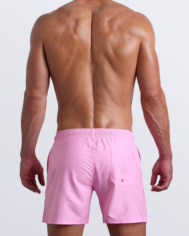Back view of a hot male model wearing men’s boardshorts in pink by the Bang! Clothes brand of men&
