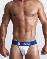 Front view of a sexy male model wearing a BANG! Cotton Jockstrap in LE MANS a solid white color with a blue waist-band with the BANG! Logo offering a perfect fit. 
