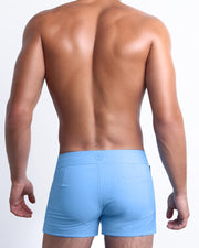 Back view of a male model wearing men’s beach trunks in carolina blue color by the Bang! Clothes brand of men's beachwear from Miami.