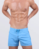 A male model wearing the MAGNET BLUE - Flex Shorts by DC2 Miami. These premium beach shorts feature a striking sky-blue color, a lace-up front, and fully-closing zip pockets for a sleek yet functional design.