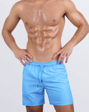 Frontal view of a sexy male model wearing the MAGNET BLUE men’s all-purpose swimwear bottoms in a solid light blue color. Designed by DC2, a premium men's beachwear brand from Miami, these stylish swim shorts feature a sleek fit, adjustable drawstring waistband, and high-performance quick-dry fabric for ultimate comfort and versatility.