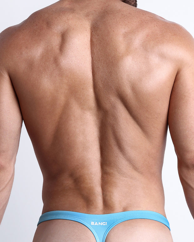 Back view of a male model wearing men’s MAGNET BLUE swim thong in blue color made with Italian-made Vita By Carvico Econyl Nylon with official logo of BANG! Brand in white.