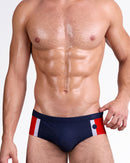DC2 Maritime Swim Brief — front view featuring solid navy blue base with bold red and white vertical side stripes, low-rise tailored fit and smooth waistband finish.
