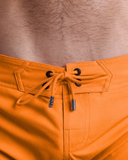 Close-up view of men’s summer Flex shorts by DC2 clothing brand, showing orange color cord with custom-branded silver cord ends, and matching custom eyelet trims in black.
