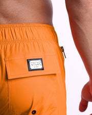 Close-up view of the MATCH POINT ORANGE men’s Flex Shorts back pocket, showing custom branded silver metal logo.