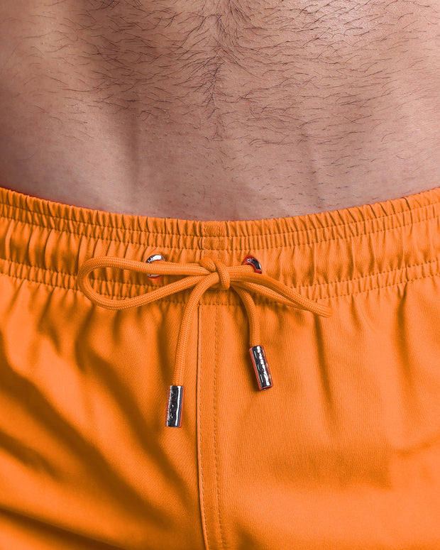 Close-up view of the MATCH POINT ORANGE men’s summer shorts, showing orange cord with custom branded silver cord ends, and matching custom eyelet trims in silver.