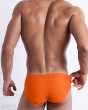 Back view of male model wearing the MATCH POINT ORANGE beach briefs for men by BANG! Miami in a solid bright orange color.
