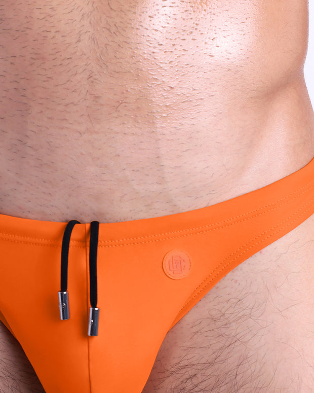 Close-up view of the MATCH POINT ORANGE men’s drawstring briefs showing black cord with custom branded metallic silver cord ends, and matching custom eyelet trims in silver.