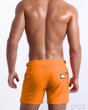 Male model wearing men’s MATCH POINT ORANGE Summer Tailored Shorts swimsuit in a solid bright orange color, complete with a back zippered pocket, designed by DC2 a BANG! Clothes capsule brand in Miami.