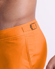 Close-up view of the MATCH POINT ORANGE men’s swimwear, showing custom branded silver metal adjustable side buckles.