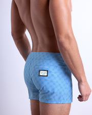 Back view of a male model wearing men’s Summer MONO BLUE Beach Shorts  in a light blue color with a darker blue monogram logo, complete with a back pocket, designed by DC2. made by DC2 a capsule brand by BANG! Clothes in Miami.