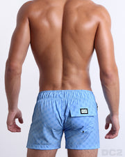 Back view of a male model wearing men’s MONO BLUE Flex Shorts swimsuits featuring the DC2 logo motif, these shorts were designed by DC2 in Miami.