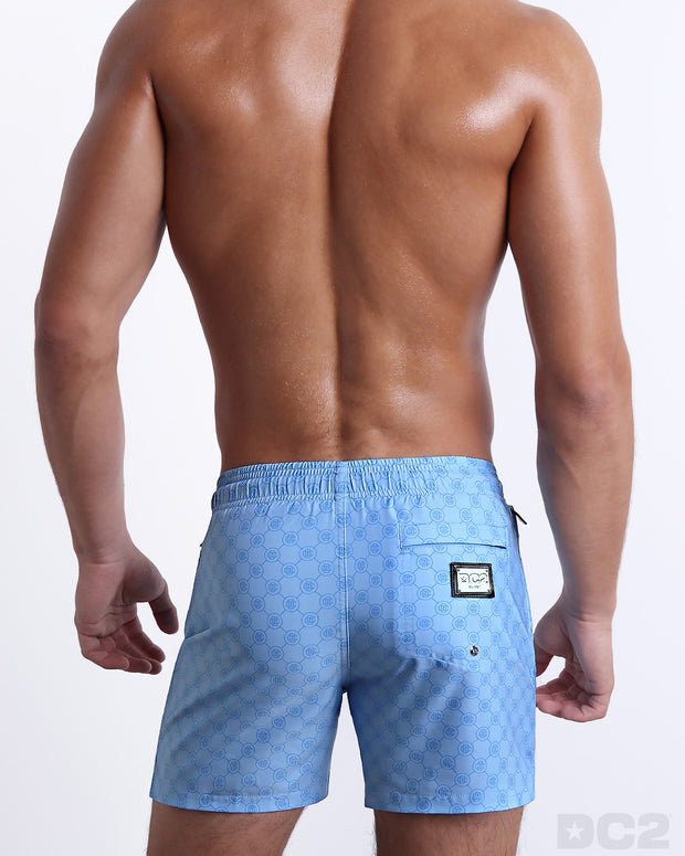 Back view of the MONO BLUE beach Resort Shorts in a light blue color with a darker blue monogram logo, complete with a back pocket, designed by DC2. 