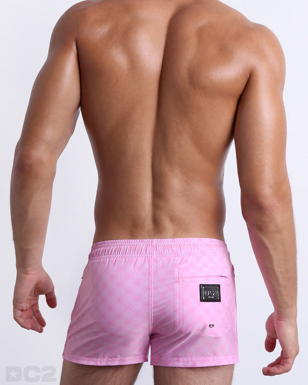 Back view of the MONO PINK beach Poolside Shorts in a light pink color with a darker pink monogram logo, complete with a back pocket, designed by DC2. 