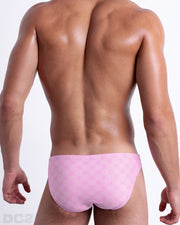 Back view of male model wearing the MONO PINK beach mini-briefs for men, with a stylish DC2 logo monogram motif in a pink print, designed by DC2.