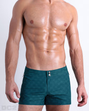 Male model wearing MONO TEAL Beach Shorts, premium swimwear with a stylish DC2 logo monogram motif in teal for men. These high-quality swimwear bottoms by DC2, a men’s beachwear brand from Miami..