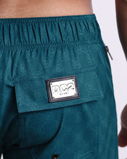 Close-up view of the MONO TEAL men’s Flex Boardshorts back pocket, showing custom branded silver metal logo.