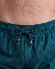 Close-up view of the MONO TEAL men’s summer shorts, showing teal blue cord with custom branded silver cord ends, and matching custom eyelet trims in silver.