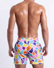 Back view of a male model wearing men’s MOSAIC beach Resort Shorts swimsuits a retro abstract colorful mosaic pattern, designed by BANG! Clothes in Miami.