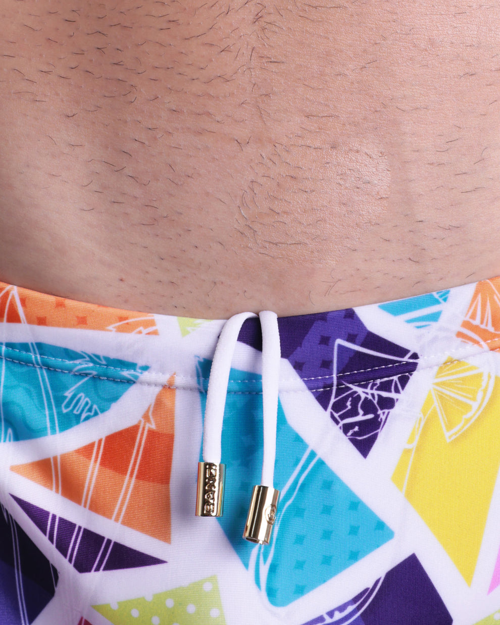 Close-up view of the MOSAIC men’s drawstring swimsuit showing white cord with custom branded golden cord ends, and matching custom eyelet trims in gold.